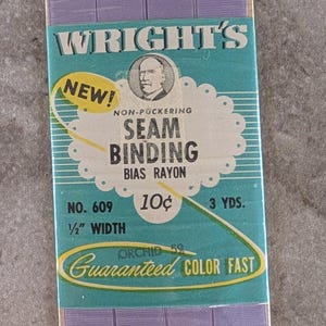 May include: A package of Wright's non-puckering seam binding in orchid purple. The package has a teal and white label with text that reads "NEW!" and "Guaranteed COLOR FAST." The binding is 1/2 inch wide and 3 yards long.