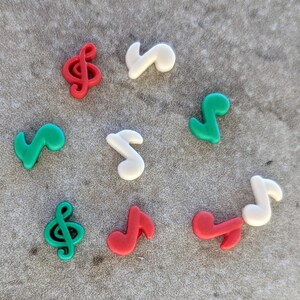 May include: A collection of eight colorful plastic musical note charms in red, green, and white. The charms are shaped like treble clefs and musical notes.