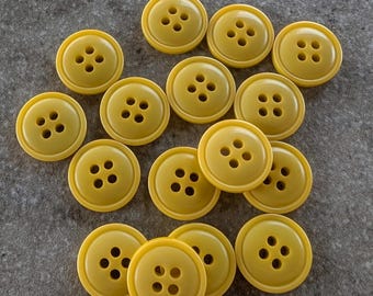 May include: A collection of round, yellow buttons with four holes each. The buttons are arranged on a gray surface, showcasing their uniform size and color. These sewing notions are ideal for various craft and apparel projects.