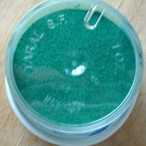 May include: A round, clear plastic container with a green, textured material inside. The container has the text "WARL 0.5" and "1.01" printed on the side.