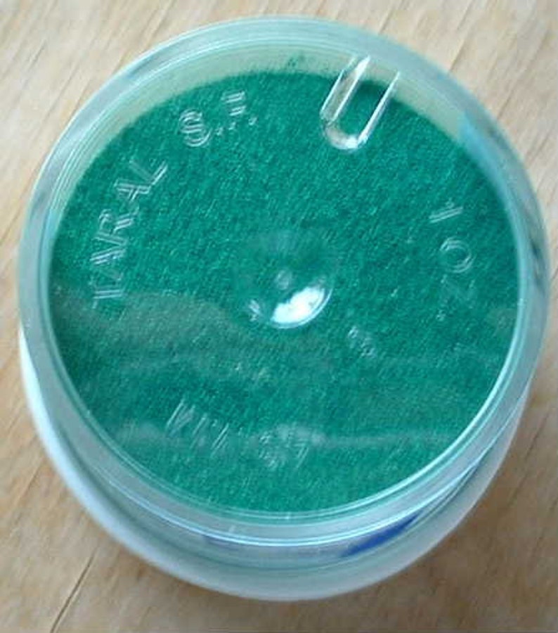 May include: A round, clear plastic container with a green, textured material inside. The container has the text "WARL 0.5" and "1.01" printed on the side.