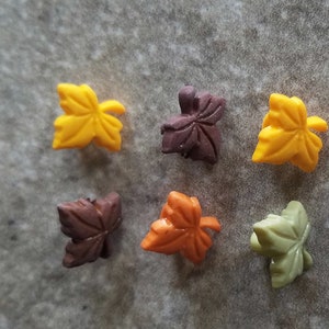 May include: Six colorful leaf-shaped buttons in various shades of yellow, orange, brown, and green. These buttons are perfect for adding a touch of autumn to crafts and sewing projects.