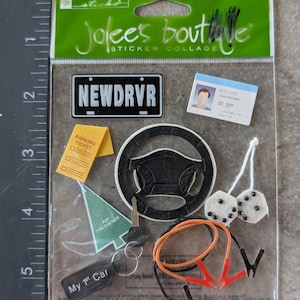 May include: A sticker collage featuring car-themed elements. Includes a license plate that reads "NEWDRVR", a steering wheel, a parking ticket, a driver's license, a key, dice, jumper cables, and an air freshener. The text "My 1st Car" is also visible.