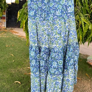 Peut inclure: Jupe à volants avec un motif floral bleu et blanc, suspendue à un cintre en bois. La jupe présente un motif répété de fleurs et de feuilles stylisées dans des tons de bleu et de vert. La jupe est en tissu léger.