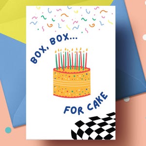 May include: A birthday greeting card with a yellow cake illustration and the text "BOX, BOX... FOR CAKE". The card is inside a blue envelope with a yellow interior, on a pink background with confetti.