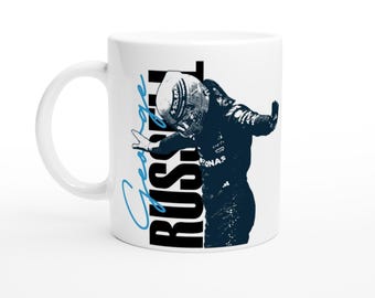 May include: White ceramic mug featuring a black and blue graphic of a race car driver with the name "George Russell" in blue script and bold black letters. The mug has a curved handle and a glossy finish.