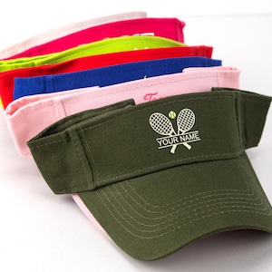 Pode incluir: Uma pilha de seis viseiras em verde-oliva, rosa claro, azul royal, vermelho, amarelo neon e branco. A viseira verde-oliva na frente apresenta um gráfico bordado de duas raquetes de tênis cruzadas com uma bola e o texto YOUR NAME.