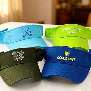 Peut inclure: Quatre visières de couleur bleu clair, vert citron, vert olive et bleu roi. La visière bleu clair présente des clubs de golf croisés et les lettres S T. La visière vert citron porte le texte Embroidery Here. La visière vert olive montre deux raquettes de tennis, une balle et le texte YOUR NAME. La visière bleu roi affiche une icône de soleil et le texte COOLE HAT.