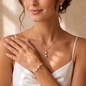 Könnte beinhalten: Ein Goldschmuckset bestehend aus einer Halskette, einem Armband und Ohrhängern. Jedes Stück verfügt über eine zarte Goldkette oder Fassung, die mit kleinen weißen Perlen und klaren, marquise-geschliffenen Steinen in Blattform verziert ist.