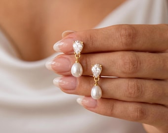 May include: A pair of gold drop earrings featuring a pear-shaped clear gemstone at the top and a white teardrop-shaped pearl suspended below. The earrings are crafted with a gold setting that connects the faceted stone to the smooth pearl drop.