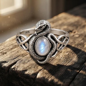 Può includere: Un anello in argento con un design a serpente avvolto, scaglie dettagliate e un cabochon ovale di pietra di luna al centro. La fascia presenta un intricato motivo a intreccio su entrambi i lati e l'interno è chiaramente marchiato con 925.