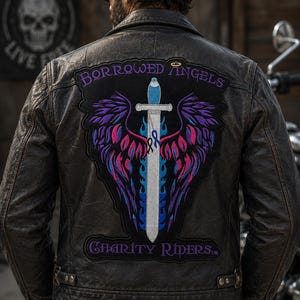 May include: A black leather jacket featuring a large embroidered back patch. The patch displays a silver sword with blue flames, purple and pink wings, and the text "BORROWED ANGELS" at the top and "CHARITY RIDERS" at the bottom in purple lettering.