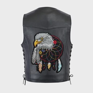 Può includere: Un gilet in pelle nera con una grande toppa ricamata sul retro. La toppa raffigura una testa d'aquila dettagliata integrata in un design colorato di acchiappasogni, completo di piume pendenti nelle tonalità del giallo, beige e azzurro.