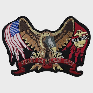 May include: An embroidered patch featuring a bald eagle with spread wings, a tattered American flag on the left, and the Marine Corps emblem on the right. A red banner across the bottom displays the text FIRST IN LAST OUT in gold lettering.