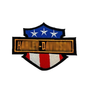 May include: A Harley-Davidson patch with a shield design. The top section is blue with three white stars. The centre has a rectangular section with the brand name, and the bottom has red and white stripes.