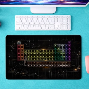 Puede incluir: Alfombrilla de ratón rectangular negra con un diseño colorido de la tabla periódica de los elementos. Se ven un teclado blanco, un ratón rosa y accesorios de escritorio sobre una superficie turquesa.