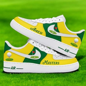 May include: White, yellow, and green sneakers with golf-themed graphics. One shoe has "Amen", the other "Masters". Each shoe features a golf ball and flag design. The soles display "AIR". The sneakers are set against a green background.