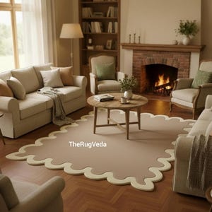 May include: A living room scene featuring a beige rug with a scalloped edge, a wooden coffee table, and a fireplace. The room includes beige sofas, armchairs, and a bookshelf, creating a cozy and inviting atmosphere.