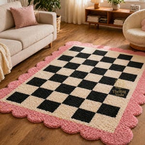 May include: A rectangular rug with a checkerboard pattern in black and cream, framed by a scalloped pink border. The rug is placed on a wooden floor, and the design adds a playful touch to the room's decor.