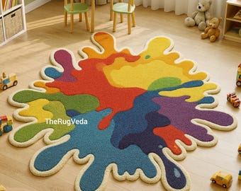 May include: A colorful, splash-shaped rug with a cream-colored border. The rug features a vibrant mix of colors, including red, yellow, blue, green, and purple. The rug is placed on a light-colored wooden floor in a child's playroom.