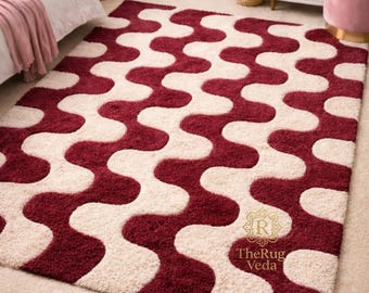 May include: A rectangular area rug with a repeating wavy pattern in burgundy and cream. The rug has a plush texture and is placed on a light beige carpet. The logo "TheRug Veda" is visible in the bottom right corner.