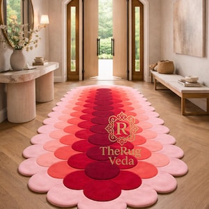 May include: An elongated oval rug featuring a scalloped edge and a gradient pattern of circular shapes in shades of deep red, bright red, and light pink. The center of the rug displays a gold logo with the text TheRug Veda in a serif font.