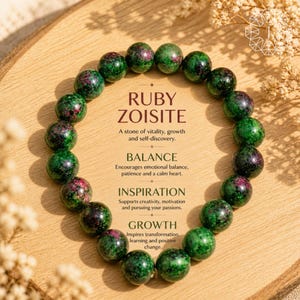 May include: A beaded bracelet made of green and red ruby zoisite stones. The image includes text describing the stone's properties: vitality, growth, balance, inspiration, and growth. The bracelet is displayed on a wooden surface.