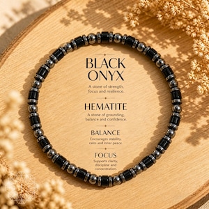 May include: A black onyx and hematite beaded bracelet. The bracelet features black and silver beads. Text on the image reads "Black Onyx", "Hematite", "Balance", and "Focus". The bracelet is displayed on a wooden surface.
