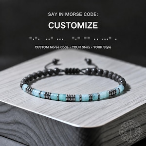 May include: A beaded bracelet with a dark grey cord and beads. The bracelet features light blue and silver-colored beads. The text on the image says "SAY IN MORSE CODE: CUSTOMIZE". Below the text, it says "CUSTOM Morse Code • YOUR Story • YOUR Style".