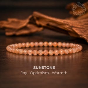 Puede incluir: Una pulsera de cuentas hecha de pequeñas cuentas redondas y translúcidas de piedra solar de color melocotón. El texto SUNSTONE Joy · Optimism · Warmth está impreso en blanco debajo de la pulsera. Las cuentas tienen un brillo sutil.