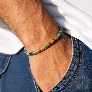 May include: A beaded bracelet featuring a sequence of cylindrical turquoise-colored stone beads interspersed with smooth, cylindrical wooden beads and small metallic spacers, arranged in a repeating pattern around the wrist.