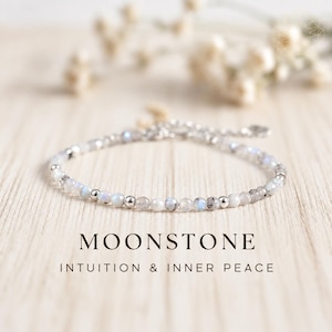 May include: A delicate bracelet featuring small, faceted moonstone beads interspersed with tiny, polished silver-tone metal spheres. The text MOONSTONE INTUITION & INNER PEACE is printed below the jewelry piece, which has a silver-tone clasp.