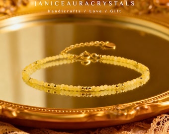 May include: A delicate yellow beaded bracelet with gold accents, resting on a reflective surface. The bracelet features small, round yellow beads and gold-colored metal beads. The image includes the text "JANICEAURACRYSTALS handicrafts / Love / Gift".
