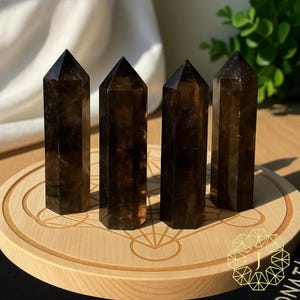 May include: Four dark brown, faceted crystal towers with pointed tops are displayed on a light wooden, circular stand. The crystals have a translucent quality, and the stand features an engraved geometric design.