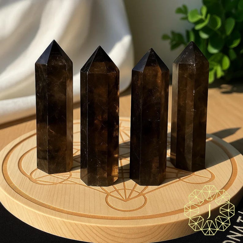 May include: Four dark brown, faceted crystal towers with pointed tops are displayed on a light wooden, circular stand. The crystals have a translucent quality, and the stand features an engraved geometric design.