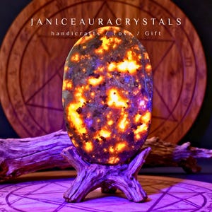 May include: An oval-shaped crystal with a fiery orange and blue pattern, displayed on a wooden stand. The crystal is the focal point, with the text "JANICEAURACRYSTALS handicrafts / Love / Gift" above it. The background includes a wooden circular design.
