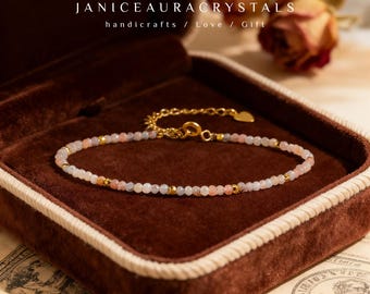 May include: A delicate bracelet with small, light pink and white beads and gold accents. The bracelet is displayed in a brown velvet jewelry box. The text "JANICEAURACRYSTALS handicrafts / Love / Gift" is at the top.