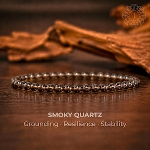 May include: A bracelet composed of small, round, translucent brown smoky quartz beads arranged in a circular formation. The text SMOKY QUARTZ Grounding · Resilience · Stability is printed in white below the bracelet on the dark surface.
