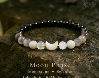 Könnte beinhalten: Ein Perlenarmband mit schwarzen, schillernden und weißen runden Perlen sowie einem zentralen weißen Halbmond-Anhänger. Der Text auf dem Bild lautet: Moon Phase, Moonstone, Selenite, Labradorite, Mother of pearl.