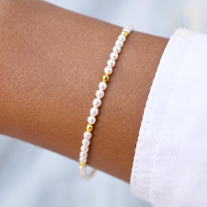 May include: A delicate bracelet featuring a single strand of small, round white pearls interspersed with polished gold-toned spherical beads. The design alternates between the white pearls and the metallic gold accents, creating a simple, uniform pattern.