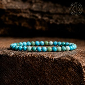 May include: A beaded bracelet composed of small, round, polished turquoise-colored stones in varying shades of blue and green. The beads are uniform in size and arranged in a single continuous strand, creating a circular shape on a dark surface.