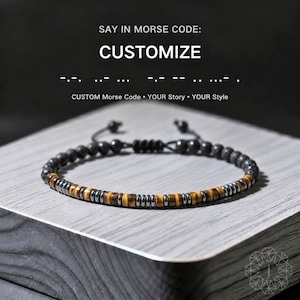 May include: A beaded bracelet featuring a mix of dark grey matte beads and a central section of alternating brown tiger eye and metallic grey cylindrical beads. The text reads: SAY IN MORSE CODE: CUSTOMIZE, followed by Morse code and CUSTOM Morse Code.