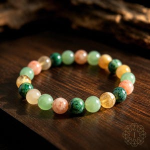 May include: A beaded bracelet featuring a circular arrangement of polished, spherical gemstones in alternating shades of translucent yellow, opaque forest green, and soft peach. The beads are strung together on an elastic cord, creating a continuous loop.