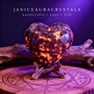 May include: A heart-shaped crystal with orange and brown patterns, displayed on a wooden stand. The crystal is set on a wooden base with a carved design. The image includes the text "JANICEAURACRYSTALS" and the words "handicrafts / Love / Gift".
