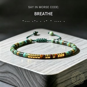May include: A beaded bracelet with turquoise, brown, and gold accents. The bracelet features a sliding knot closure and the words "SAY IN MORSE CODE: BREATHE" above it. The beads are strung on a green cord.