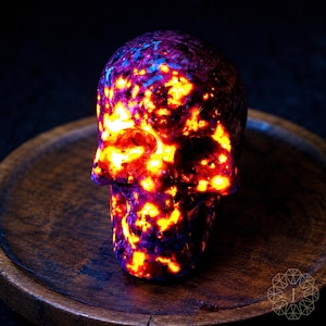 May include: A glowing skull sculpture with a fiery, multi-colored pattern of orange, yellow, purple, and blue. The skull is set on a dark wooden plate, creating a striking contrast. The intricate details of the skull are highlighted by the vibrant colors.