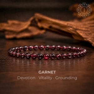May include: A beaded bracelet made of small, round, deep red garnet gemstones. The text GARNET, Devotion, Vitality, Grounding is printed below the bracelet. The beads have a smooth, polished finish and are arranged in a single circular strand.