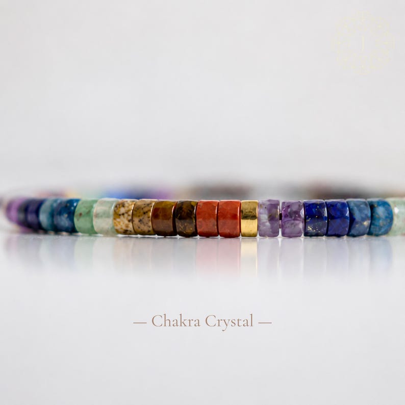 May include: A bracelet composed of small, cylindrical, multi-colored gemstone beads arranged in a sequence of purple, blue, green, tan, brown, orange, red, gold, and violet hues. The text "Chakra Crystal" is printed below the bracelet.