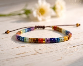 May include: A bracelet featuring small, flat, circular beads in a variety of colors including red, orange, yellow, green, blue, and purple, arranged in a repeating pattern. The bracelet includes a brown cord with adjustable sliding knots.