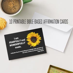 May include: A black affirmation card with a yellow sunflower and the text "I am fearfully and wonderfully made." The card is part of a set of 10 printable Bible-based affirmation cards. A white envelope and a cup of coffee are also in the image.